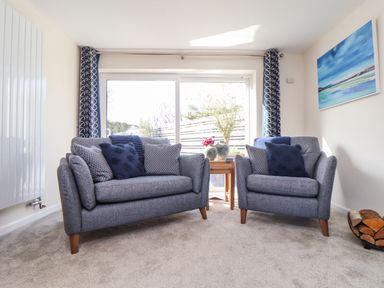 A living room with two grey sofas a wooden side table between them and blue curtains by sliding glass doors at Pickney House in Killigarth near Polperro