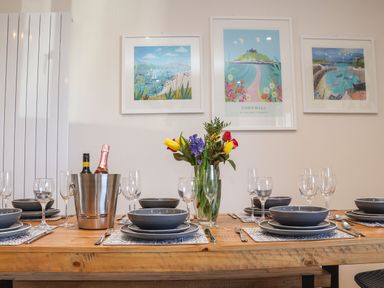 A dining table set with plates bowls glasses cutlery and a flower vase with paintings on the wall at Pickney House Killigarth near Polperro
