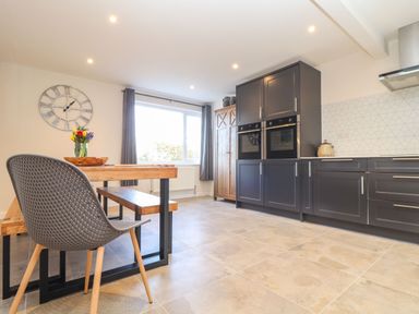 A kitchen with a dining table, chairs, cabinets, and a large wall clock at Pickney House in Killigarth near Polperro