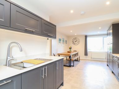 A kitchen with gray cabinets a sink and a wooden dining table with bench seating at Pickney House in Killigarth near Polperro