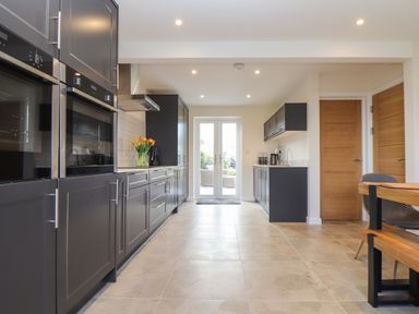 A kitchen with dark cabinets and built in ovens with glass doors and a wooden table at Pickney House in Killigarth near Polperro