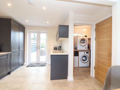 A kitchen with dark cabinets a sink and a utility room with stacked washer and dryer at Pickney House in Killigarth near Polperro