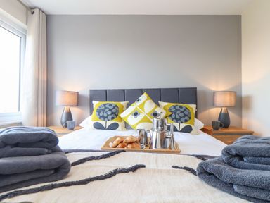 A bedroom with a bed with patterned pillows lamps on bedside tables and folded towels at Pickney House in Killigarth near Polperro