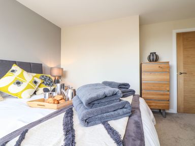 A bedroom with a bed with folded towels a tray with croissants and tea set a wooden chest of drawers and a door at Pickney House in Killigarth near Polperro