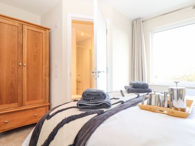 A bedroom with a wooden wardrobe a bed with folded towels and a tray with a tea set by Pickney House in Killigarth near Polperro
