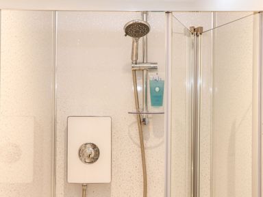 A shower area with a handheld showerhead and a bottle of shower gel in a glass shelf at Pickney House in Killigarth near Polperro