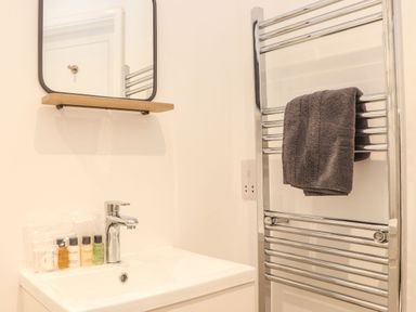 A bathroom sink with toiletries under a mirror and a heated towel rail with a dark towel at Pickney House Killigarth near Polperro