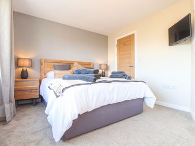 A bedroom with a bed with wooden headboard bedside tables lamps a door and a wall mounted television at Pickney House in Killigarth near Polperro