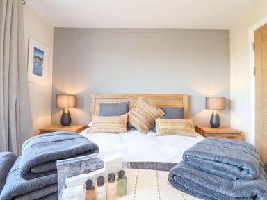 A bedroom with a wooden bed frame bedside tables lamps folded towels and toiletries at Pickney House in Killigarth near Polperro