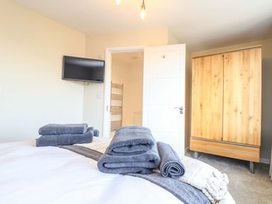 A bedroom with folded towels on the bed a wooden wardrobe and a wall-mounted television at Pickney House in Killigarth near Polperro
