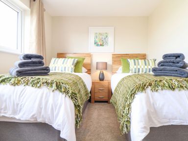 A bedroom with two single beds side by side each with green throws pillows and folded towels on Pickney House in Killigarth near Polperro
