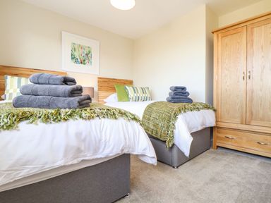 A bedroom with two single beds with folded towels and green throws and a wooden wardrobe at Pickney House in Killigarth near Polperro