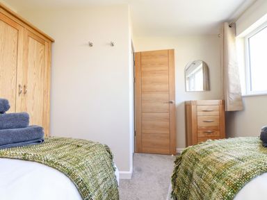 A bedroom with two beds green woven blankets wooden wardrobe chest of drawers and a window at Pickney House in Killigarth near Polperro