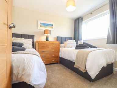 A bedroom with two single beds a wooden chest of drawers and a window with curtains at Pickney House in Killigarth near Polperro