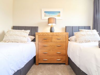A bedroom with two single beds and a wooden dresser with a lamp between them at Pickney House in Killigarth near Polperro