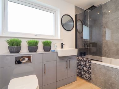 A bathroom with a toilet sink gray cabinets three plants and a bathtub with a shower at Pickney House Killigarth near Polperro
