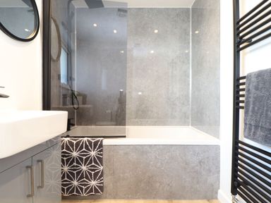 A bathroom with a bathtub shower combination a gray patterned towel a white sink and a black towel rack at Pickney House in Killigarth near Polperro