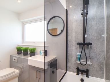 A bathroom with a bathtub, shower, sink, toilet, and three small plants on a cabinet at Pickney House in Killigarth near Polperro