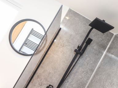 A bathroom shower area with a black showerhead and a round mirror reflecting a towel radiator at Pickney House in Killigarth near Polperro