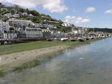 A harbor with boats moored along a waterfront with buildings on a hillside at Pickney House in Killigarth near Polperro