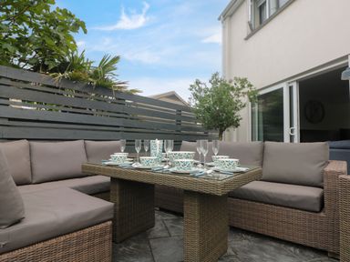 An outdoor patio area with a wicker dining table and cushioned seating with tableware and glassware at Pickney House in Killigarth near Polperro