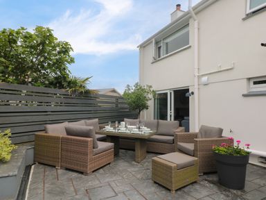An outdoor patio with brown wicker chairs and sofas around a table set with dishes and glasses at Pickney House in Killigarth near Polperro