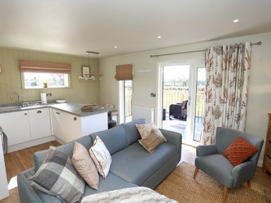 A living room with a blue sofa and armchair next to a kitchen and patio doors at The Swift in Wem