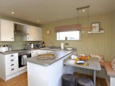 A kitchen with white cabinets a countertop dining area with stools and a breakfast table at The Swift in Wem