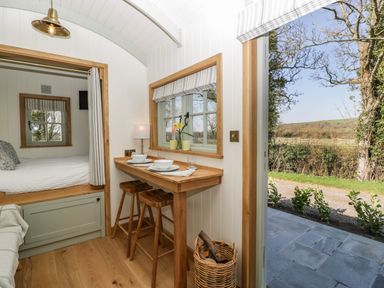 A small dining area with two wooden stools and a built-in bed next to an open door showing an outdoor view at Acorn in Bleadon