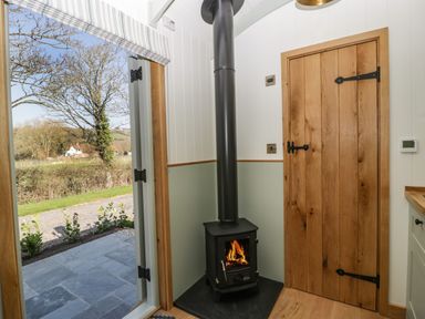 A corner with a wood burning stove and a wooden door next to an open door showing an outside view at Acorn in Bleadon