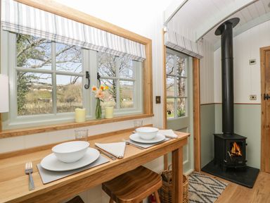 A dining area with a wooden table set for two next to windows and a wood burning stove at Acorn in Bleadon