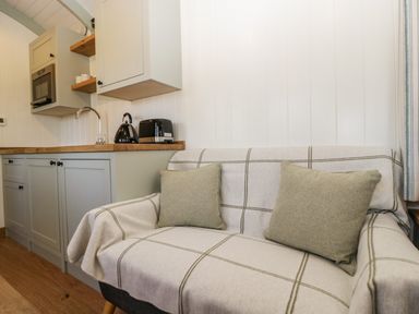A small kitchen area with a countertop kettle toaster and microwave beside a sofa with two cushions at Acorn in Bleadon