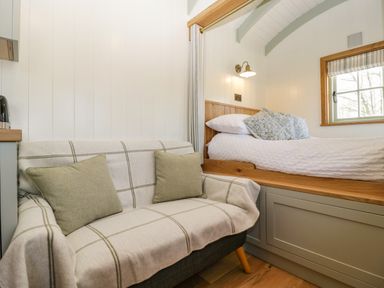 A small sitting area with a plaid covered sofa and cushions next to a wooden framed bed with pillows and a window at Acorn in Bleadon