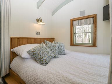 A bedroom with a bed with three pillows and a window with striped blinds at Acorn in Bleadon