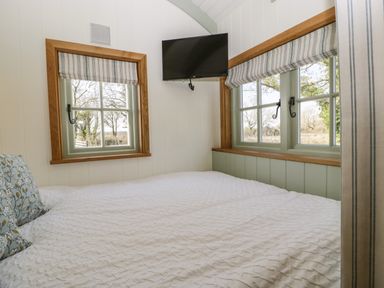 A bedroom with a bed white bedding two windows with wood trim and a mounted television at Acorn in Bleadon