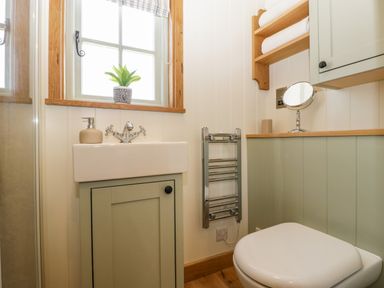 A bathroom with a sink, a toilet, a small towel rack, a window with a plant on the sill, and shelves with rolled towels at Acorn in Bleadon