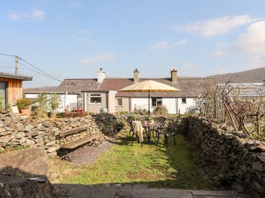 A garden with a table and chairs under an umbrella and a bench along a stone wall at 9 Ty Du Road in Llanberis