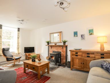 A living room with a fireplace, wooden furniture, a television, armchair, and a red rug at 9 Ty Du Road in Llanberis