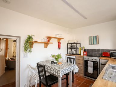 A kitchen with a table and chairs a stove a sink and shelves with kitchen items at 9 Ty Du Road in Llanberis