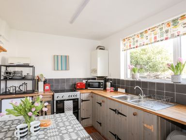 A kitchen with wooden countertops a dual sink a stove a microwave a toaster a kettle mugs flowers and a table with tulips and cups at 9 Ty Du Road in Llanberis