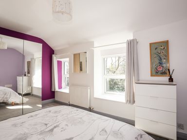 A bedroom with a bed a white dresser a window with grey curtains and a mirrored wardrobe at 9 Ty Du Road in Llanberis