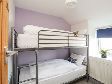 A bedroom with metal bunk beds next to a window with a blue blind and a plant on the windowsill at 9 Ty Du Road in Llanberis