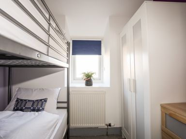 A small bedroom with a metal bunk bed a window with a blue blind a potted plant a white wardrobe and a wooden chest of drawers at 9 Ty Du Road Llanberis
