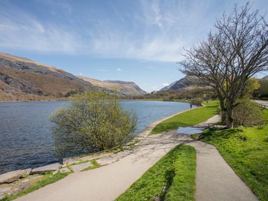 A lakeside path with trees and mountains in the background at 9 Ty Du Road in Llanberis