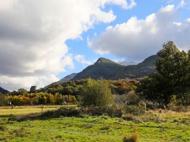 A grassy field with trees and hills under a partly cloudy sky at 9 Ty Du Road in Llanberis