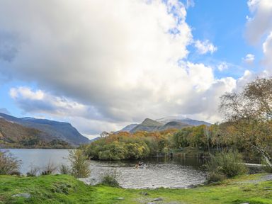 A lake with trees and mountains in the background with a person rowing a boat at 9 Ty Du Road in Llanberis