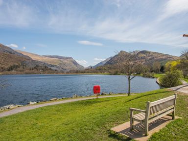 A bench near a lake with mountains in the background at 9 Ty Du Road in Llanberis