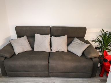 A gray sofa with four light pillows a green plant and a red dog statue with sunglasses at Sunnydene in Paignton