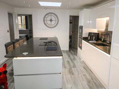 A modern kitchen with a black countertop island and stools a large wall clock and white cabinetry at Sunnydene in Paignton