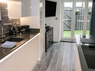 A modern kitchen with black countertop appliances a sink and glass doors leading to a garden at Sunnydene in Paignton